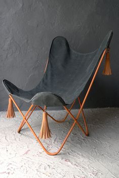 a black chair with tassels on it sitting in front of a gray wall