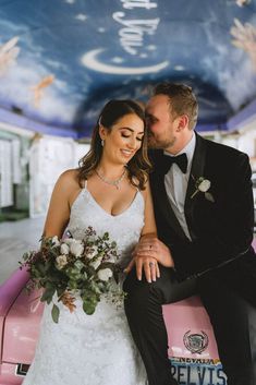 a bride and groom sitting on top of a pink car in front of a painted ceiling