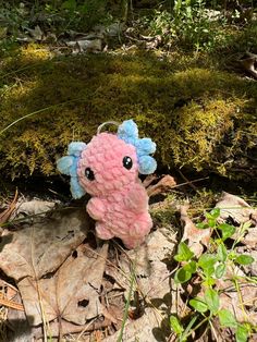 a pink and blue stuffed animal laying on the ground next to some moss covered rocks