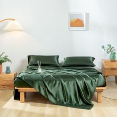 a bed with green sheets and pillows in a white room next to two wooden nightstands