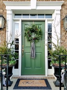 a green front door with wreaths and potted plants