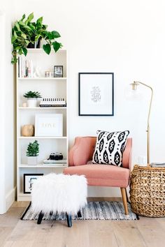 a living room with a pink chair and bookshelf filled with plants on top of it