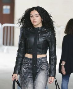 a woman walking down the street with a handbag on her shoulder and wearing a black leather jacket