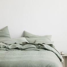 an unmade bed with green linens in a white walled room, next to a nightstand