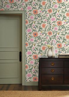 a dresser with two vases on top of it next to a wallpapered room