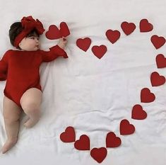 a baby laying on top of a bed with lots of red hearts in the air