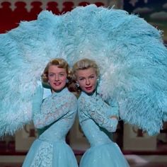 two women dressed in blue posing for a photo with large feathers on their head and arms