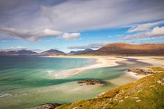 the beach is surrounded by mountains and clear blue water, with green grass on both sides