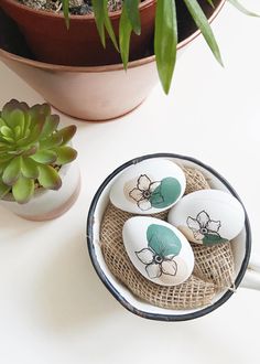 three decorated eggs sitting in a bowl next to a potted plant