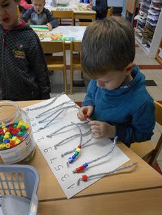 two young boys sitting at a table working on crafts with plastic beads and paper clips