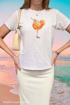 Cruise the Italian riviera in our y2k baby tee shirt with a trendy large Aperol Spritz graphic  - the perfect European summer aesthetic. This 90s baby tee shirt makes a preppy Pinterest summer outfit and better yet get a matching gift for your bestie in crime - make sure the bartender keeps the drinks coming! This minimal print top is perfect to style with your low rise jeans or skirt and y2k sunglasses for the perfect retro 2000s clothing fit. Get yours now and join the Aperol Spritz cocktail club, Cin Cin! 🍹 ------------------------------------------------------------------------------------------------------   Size guide Please take a moment to see the size chart, both in inches and cm, and measure against your favorite tee to make sure you get the best fit for you. This is a unisex st Y2k Style Summer T-shirt With Sublimation Print, Y2k Style Sublimation Print T-shirt For Summer, Y2k Summer Tops With Screen Print, Y2k Style Summer Tops With Screen Print, Y2k Style Screen Print Tops For Summer, Y2k Style Screen Print Summer Tops, Y2k Summer Screen Print Tops, Y2k Printed Crew Neck T-shirt, 90s Style Screen Print Tops For Summer