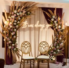 two chairs and a table in front of a wedding arch with flowers on the side