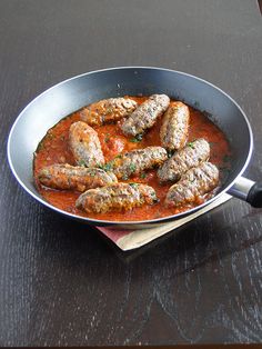 a pan filled with meatballs covered in sauce on top of a wooden table next to a knife