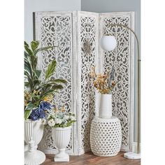 three vases with flowers in them sitting on a table next to an ornate screen