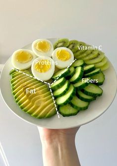 a person holding a plate with different types of food on it, including hard boiled eggs and sliced cucumbers