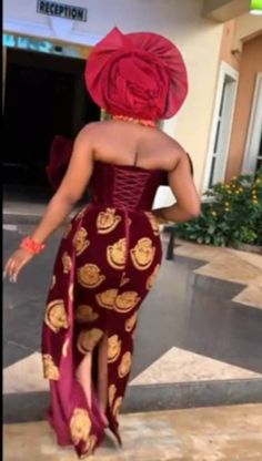 a woman in a red and gold dress is walking down the street with her back to the camera