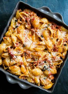 a casserole dish filled with pasta and sauce on a blue tablecloth next to a fork