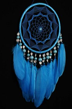 a blue dream catcher hanging on a black wall with beads and pearls in it's center