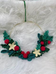 a crocheted christmas wreath with holly leaves and red berries hanging on a white furnishing