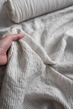 a person's hand on top of a bed with white and gray striped sheets