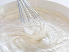 a whisk in a white bowl filled with mayonnaise and cream sauce