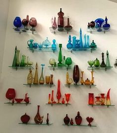 many different colored glass vases are displayed on the wall above shelves in this room