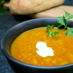 a black bowl filled with carrot soup and garnished with sour cream on top