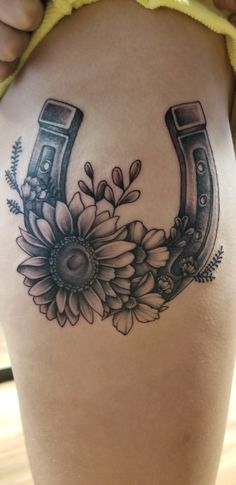 a tattoo on the back of a woman's thigh with flowers and horseshoes