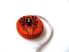 an orange tape measure with a black spider on it and a green bead in the center