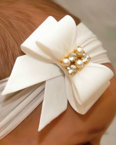 a close up of a baby's head wearing a white bow with pearls