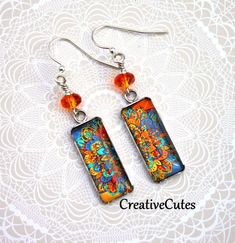 Bright orange faceted crystal beads sit atop colorful mandala art images beneath smooth glass cabochons in shiny stainless steel pendant trays...Boho Beauties! Uniquely hand crafted with these quality materials: ~ Stainless steel pendant trays with sealed images & glass cabochons ~ Silver plated lead & nickel-free French style ear wires ~ Silicone earring backs to keep earrings securely in ears Measuring 2 inches from the tops of the ear wires to the bottom of the charms, these earrings are ligh Bohemian Orange Jewelry Nickel Free, Bohemian Orange Nickel-free Jewelry, Artsy Orange Jewelry For Festivals, Artsy Orange Festival Jewelry, Colorful Artistic Dangle Jewelry, Artistic Multicolor Czech Glass Jewelry, Vibrant Orange Jewelry For Festival, Vibrant Orange Festival Jewelry, Multicolor Bohemian Glass Earrings