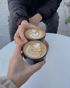 two people sitting at a table with cups of coffee in front of them, both holding their hands together