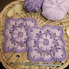 two crocheted squares sitting on top of a wicker basket next to yarn