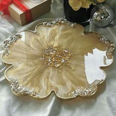 a gold flower shaped plate next to a vase with flowers in it on a white table cloth