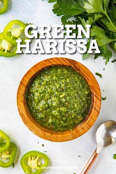 green harrisa in a wooden bowl with spoons next to peppers and cilantro