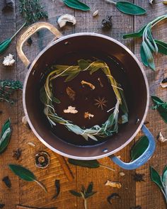 a pot filled with liquid surrounded by herbs and leaves on a wooden table, top view