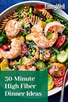 a white bowl filled with pasta, shrimp and veggies on top of a blue table