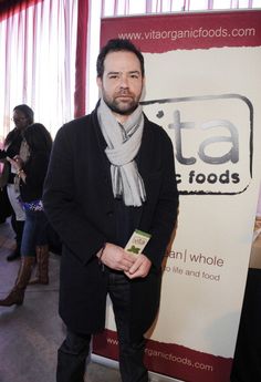 a man standing in front of a sign wearing a scarf and black jacket with his hands in his pockets