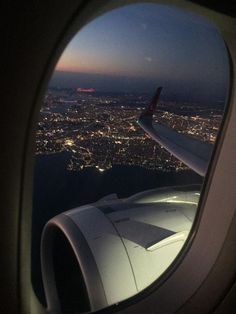 an airplane window with the view of city lights from it's wing at night