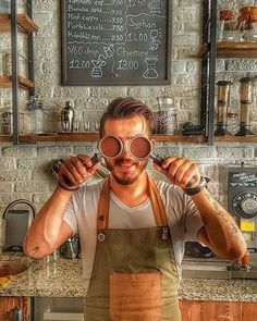 a man wearing an apron and holding up two magnifying glasses in front of his face