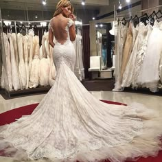 a woman in a wedding dress looking at the back of her gown while standing in front of a rack of dresses