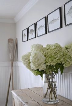 a vase filled with white flowers sitting on top of a wooden table next to pictures