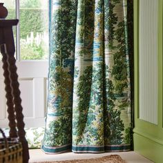 a window with green curtains and a brown rug in front of the window, next to a wooden chair