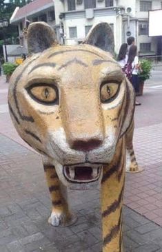 a close up of a statue of a tiger on a sidewalk with people in the background