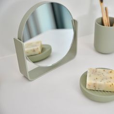 a soap bar sitting on top of a green plate next to a cup and mirror