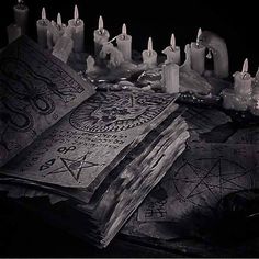 an old book is surrounded by candles and other items that are on the table in black and white