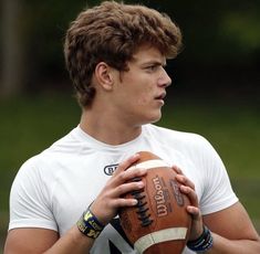 a young man holding a football in his right hand and looking at the ball with both hands