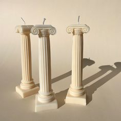 three white marble pillars with one candle on each pillar and the other in the middle