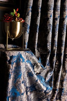 a vase with flowers sitting on top of a table next to a curtained window