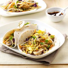 two white plates filled with tacos on top of a table next to cups and sauces